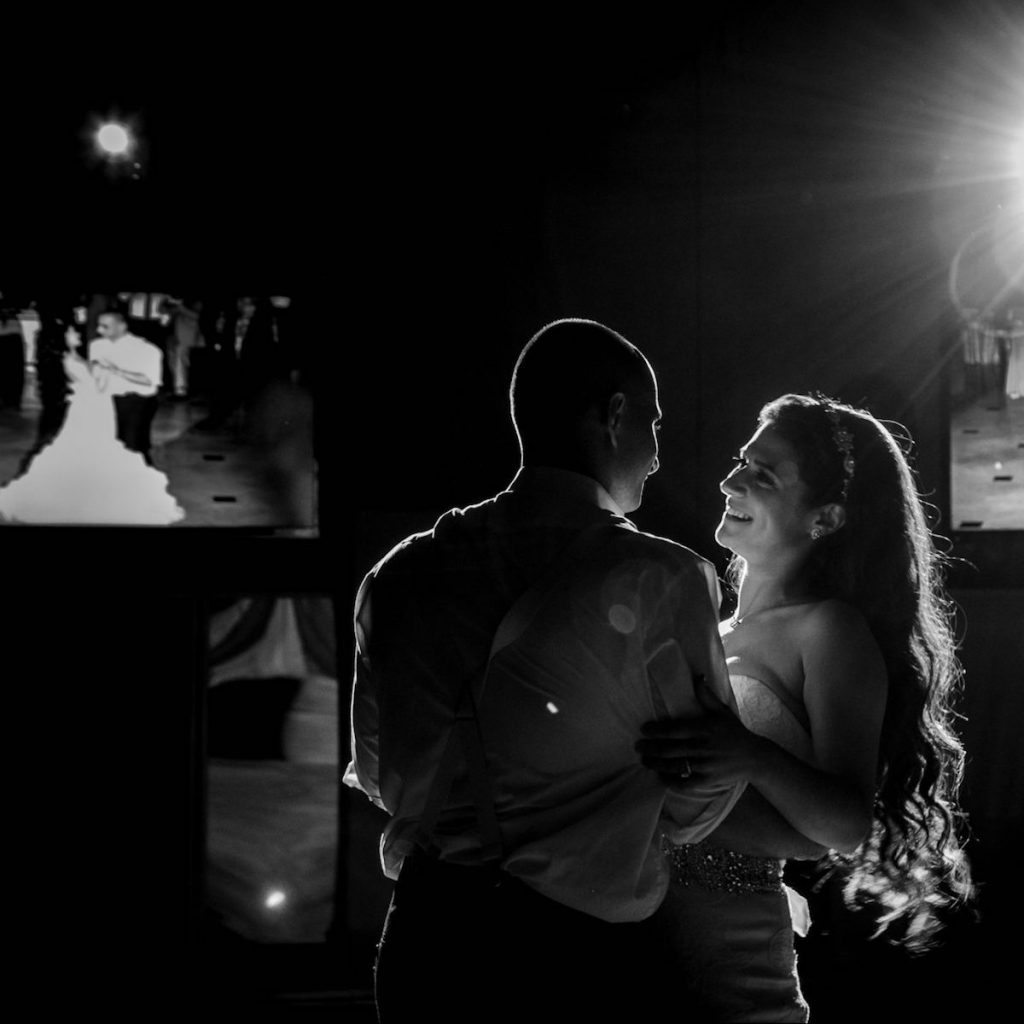 bride and groom smiling at each other with video display behind them