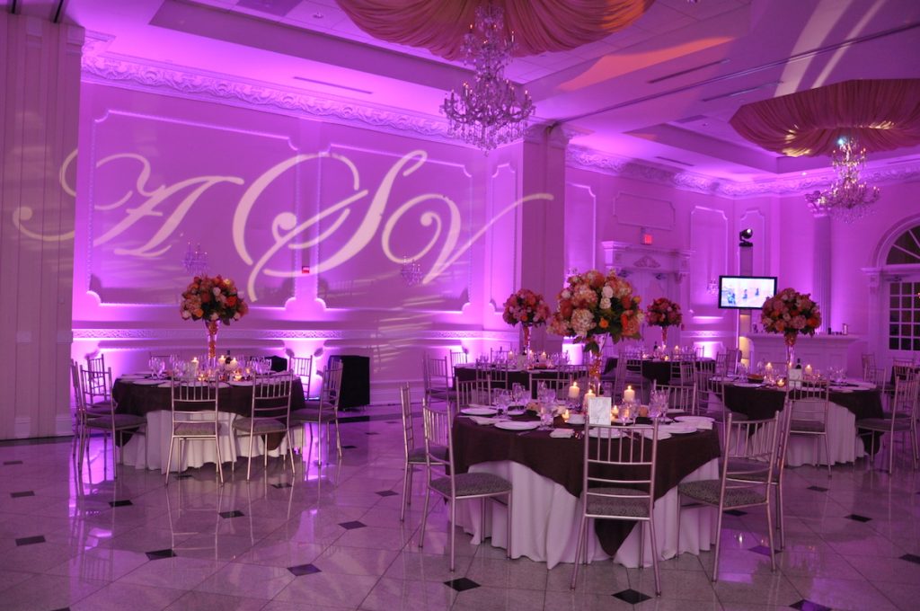 Banquet room illuminated with purple LED uplighting and custom monogram gobo